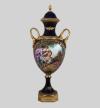 <span class='ref_item'>246 -</span> <span class="object_title">JARRÓN EN PORCELANA SÈVRES (S.XVIII)</span>   <p><span class="technical_description">Jarrón francés en porcelana Sèvres azul cobalto pintado a mano. Muestra una escena galante central firmada en la parte inferior derecha "JEANNE". Enmarcada con cenefas vegetales y motivos florales. Asas en forma de hoja de parra y tapa fija rematada con una bellota, en capas de oro. Base cuadrada en metal dorado. <br/>En la base, sello de Sèvres perteneciente la fabricación de finales del siglo XVIII, acompañado por inscripción "Peint Lamain" (pintado a mano).<br/>Medidas con base: 74x16cm</span><br></p>